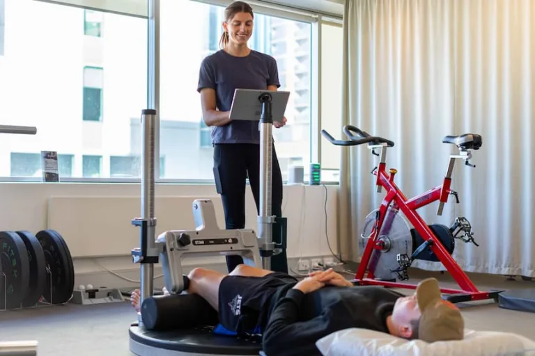 Physiotherapist recording results on a laptop while a patient completes a KangaTech strength assessment